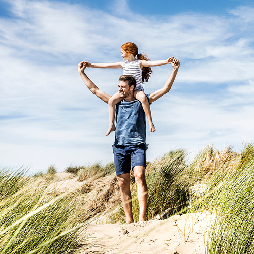 Mann trägt Tochter auf den Schultern am Strand.