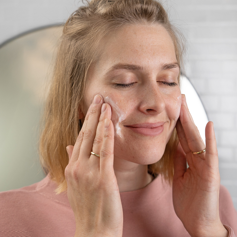 Frau cremt sich lächelnd die Wangen ein