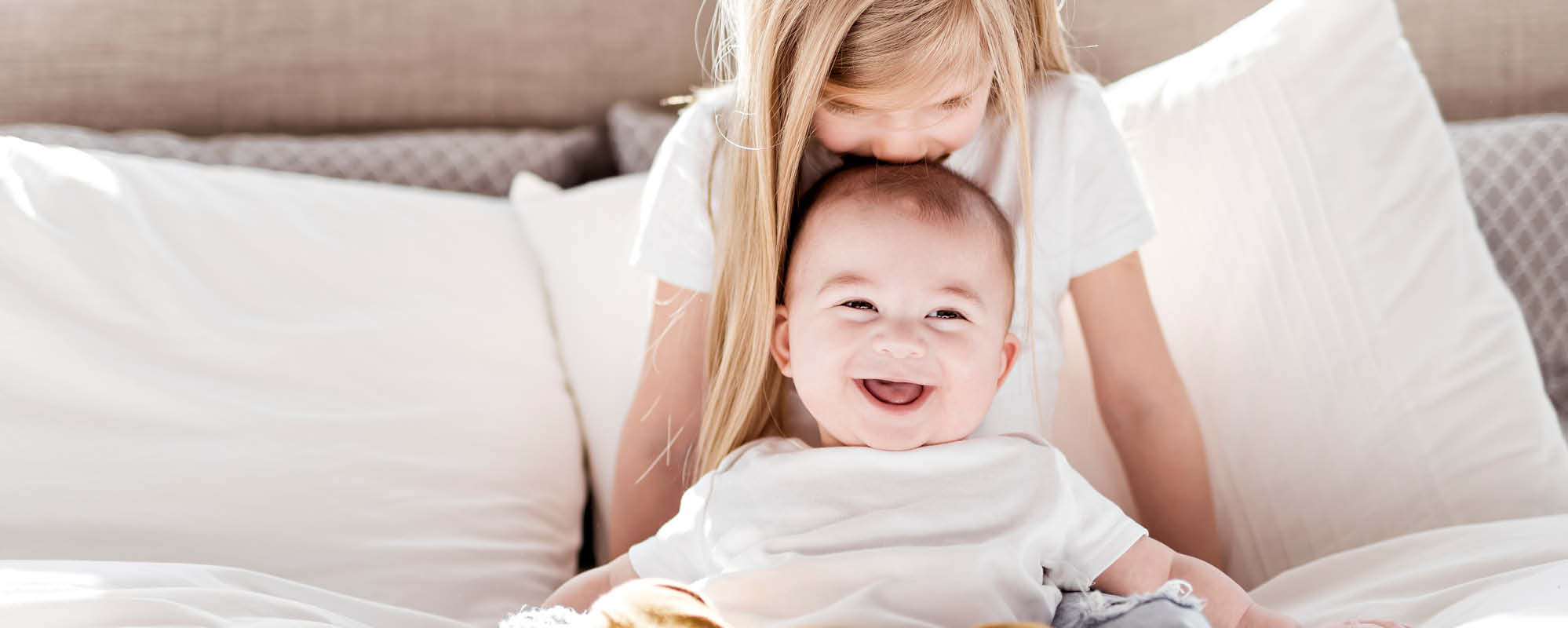 Blondes Mädchen küsst ihren Babybruder auf den Kopf