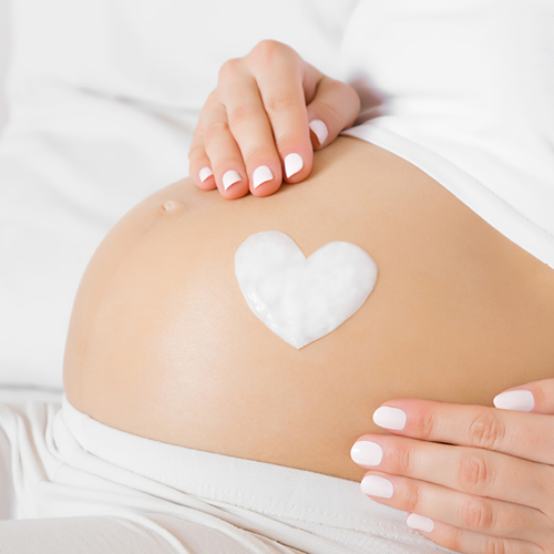Herz aus Creme auf einem schwangeren Bauch