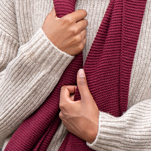 Hände halten roten, dicken Schal vor Winterpullover
