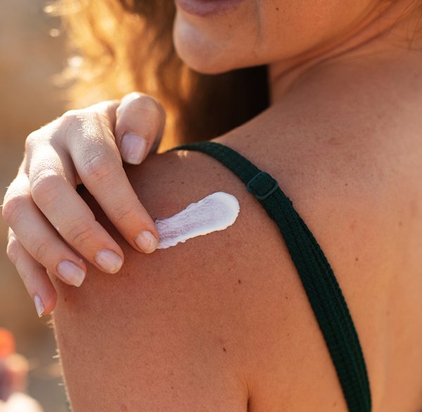 Frau cremt sich die Schulter mit Sonnencreme ein