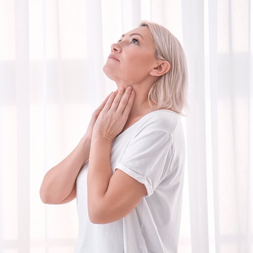 Blonde Frau tastet ihre Schilddrüse am Hals ab.