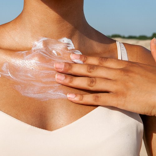 Frau cremt ihr Dekollete mit Sonnencreme ein