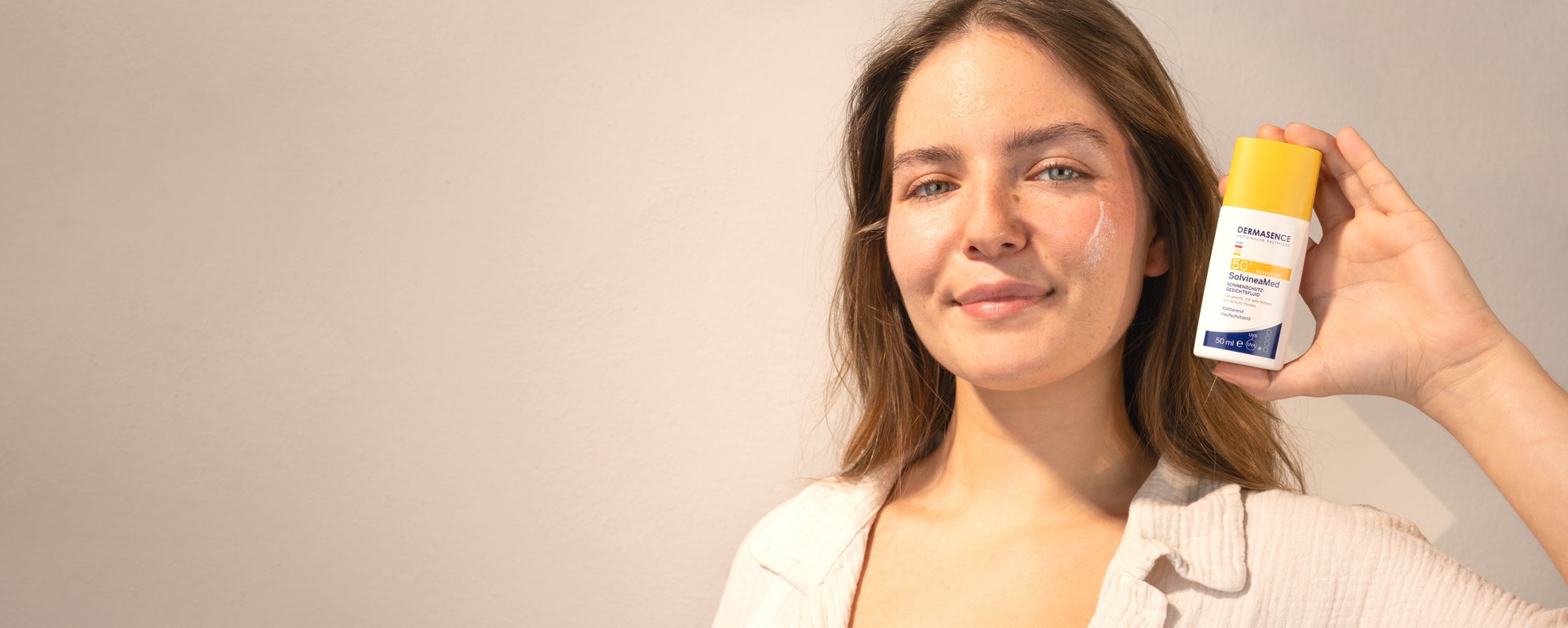 Brünette Frau hält lächelnd ein Produkt neben ihr Gesicht