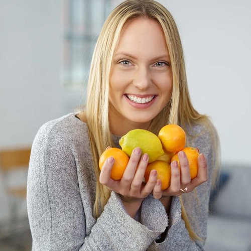 Eine blonde Frau hält mehrere Zitrusfrüchte in die Kamera.