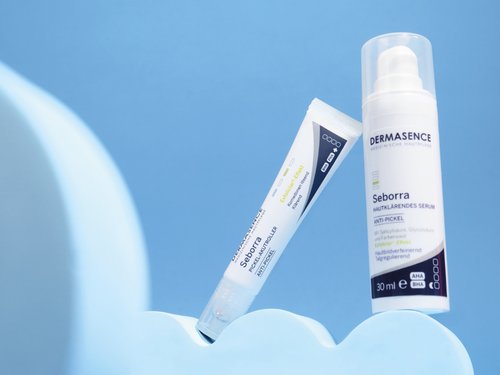 DERMASENCE Seborra Pickel-Akutroller und DERMASENCE Seborra Hautklärendes Serum vor blauem Hintergrund