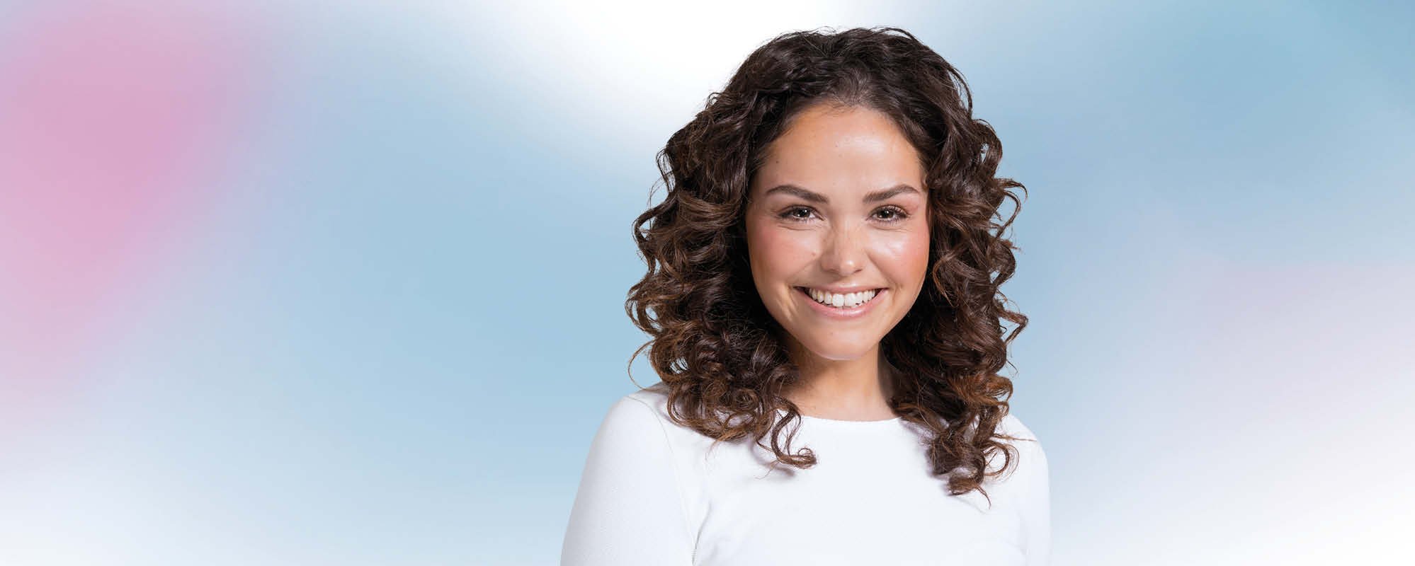 Lächelnde, junge Frau mit braunen Locken vor blau-rosa Hintergrund