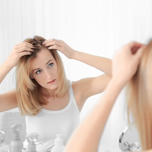 Frau betrachtet ihre Schuppenflechte auf der Kopfhaut im Spiegel