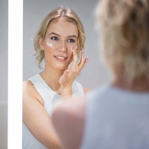 Frau trägt sich Creme auf ihre Wangen auf.