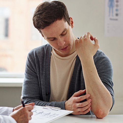 Patient, der seiner Ärztin seine Schuppenflechte zeigt.