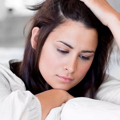 Dunkelhaare Frau sitzt betrübt auf dem Sofa