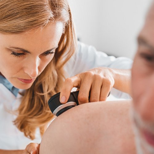 Eine Dermatologin untersucht die Schulter eines Mannes.