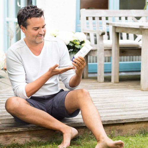 Ein Mann mittleren Alters sitzt auf der Terrasse und nutzt eine Pflegecreme.