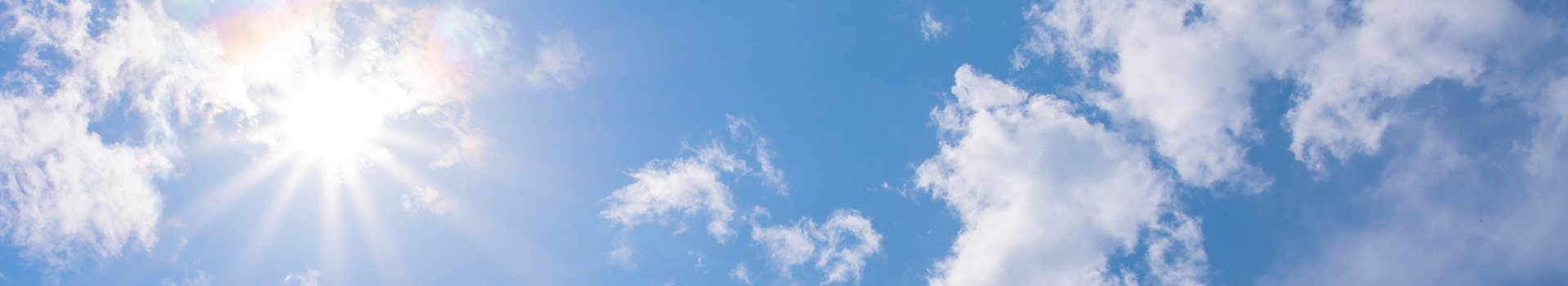 Sonne und einzelne Wolken am blauen Himmel