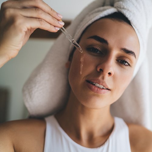 Frau träufelt mit einer Pipette ein Retinolprodukt auf ihre Wange.