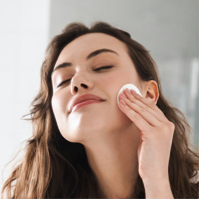 Frau reinigt ihr Gesicht mit einem Wattepad