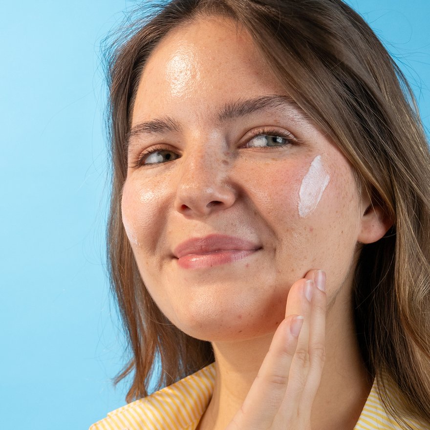 Gesicht einer lächelnden, brünetten Frau mit Creme auf der Wange