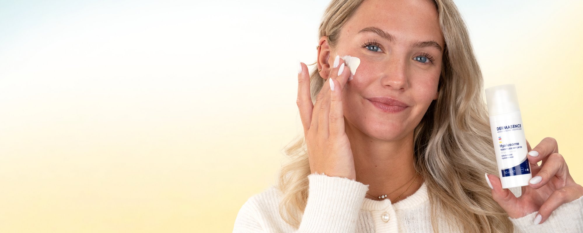 Blonde Frau trägt lächelnd Creme im Gesicht auf